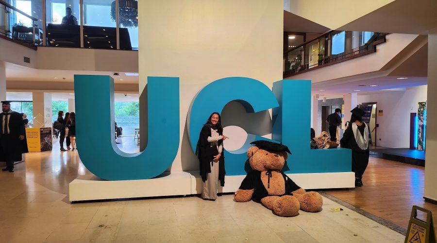 • Person standing next to large UCL sign while pointing at a big teddy bear
