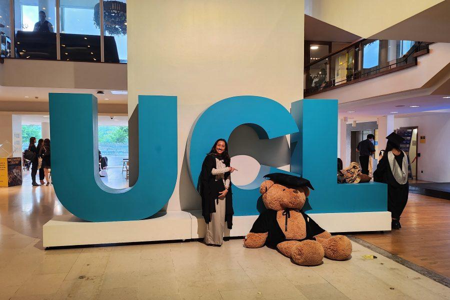 • Person standing next to large UCL sign while pointing at a big teddy bear